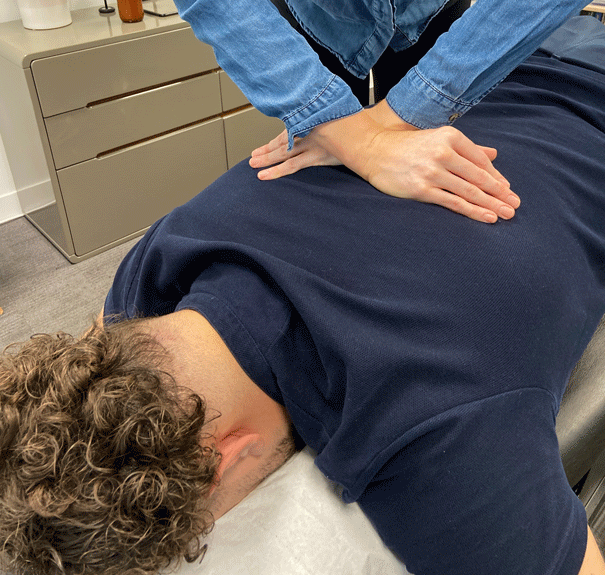 Close-up of professional massage chiropractic's hands massaging back muscles of a young man, relaxing, lying down on massage table at chiropractic clinic.